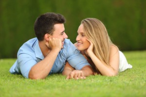 Couple in love dating and looking each other lying on the grass with a green background